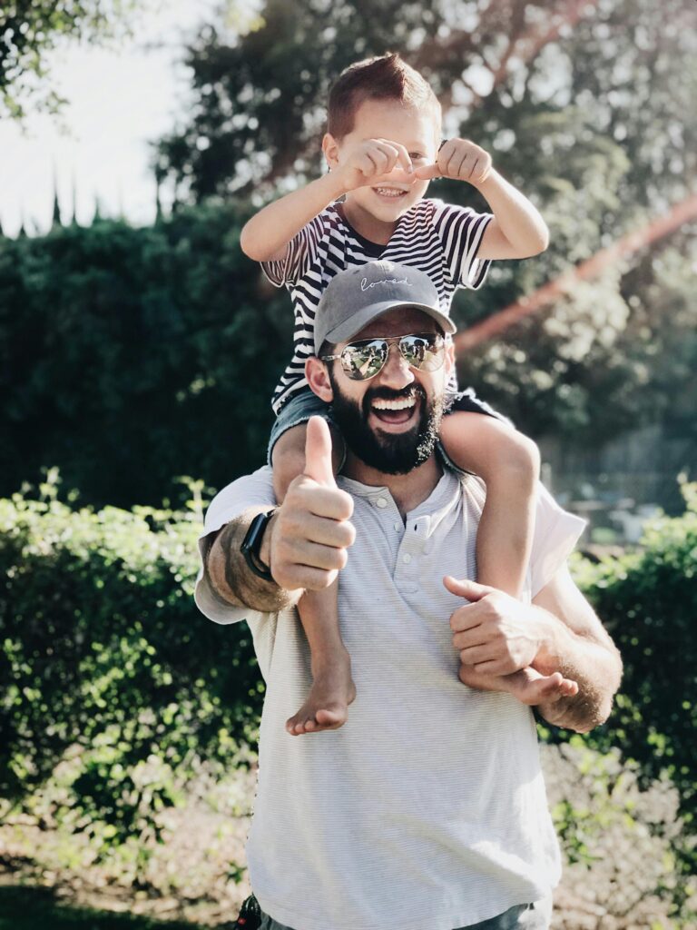 pexels-photo-1456951-1456951 Father giving son a ride on shoulders, both laughing and smiling in a park setting.