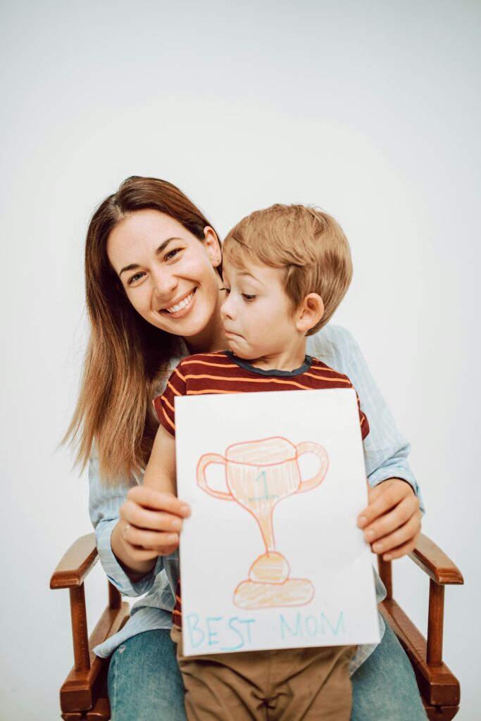 pexels-photo-7005179-7005179 Mother and son smiling with 'Best Mom' drawing on bond paper.